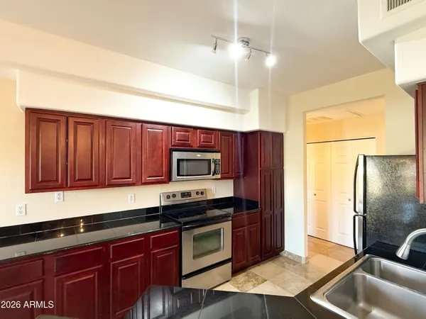 a kitchen with stainless steel appliances granite countertop a refrigerator a stove and a sink with wooden cabinets