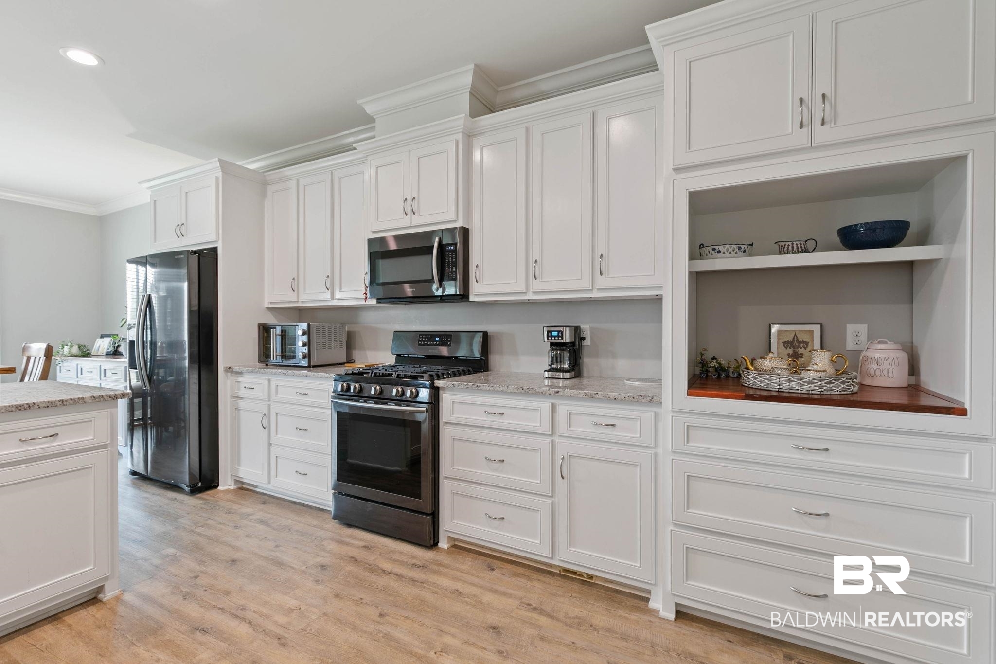 9388 Pembrook Loop Fairhope, AL 36532 - Photo 24 of 53 Kitchen featuring appliances with stainless steel finishes, crown molding, white cabinetry, light wood-style flooring, and light stone counters