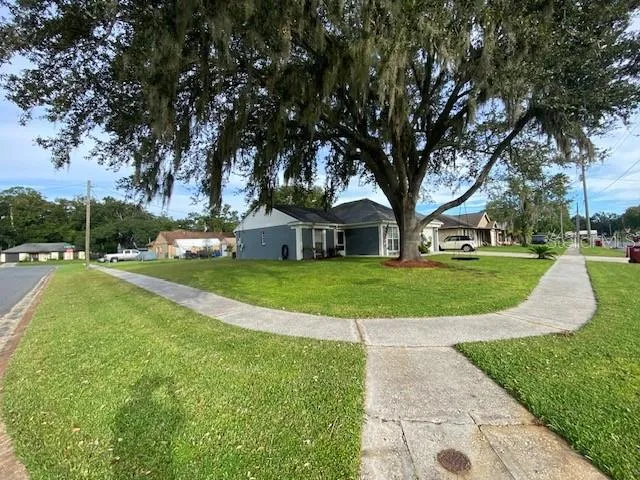 a view of a house with a big yard potted plants and large trees