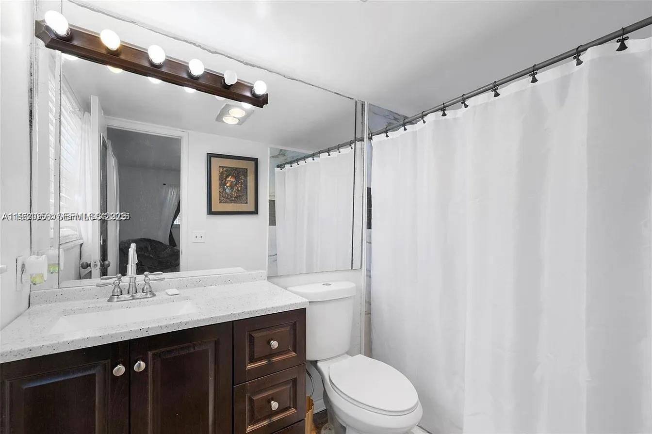 4043 Northwest 16th Street, Unit 201 Lauderhill, FL 33313 - Photo 17 of 22 a bathroom with a sink a toilet a mirror and shower curtain