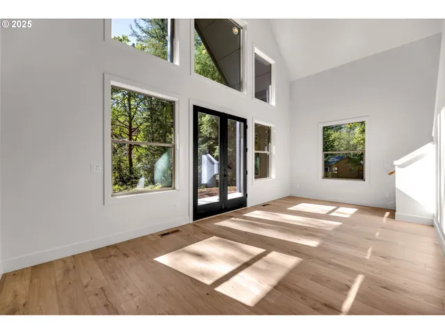 a view of an empty room with window and hardwood floor