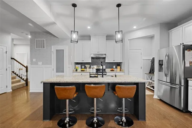 a kitchen with stainless steel appliances granite countertop a dining table chairs refrigerator and sink
