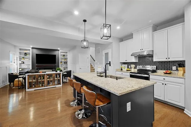 a kitchen with stainless steel appliances granite countertop a stove top oven a sink a dining table and chairs with wooden floor