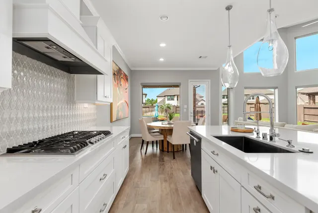 a kitchen with stainless steel appliances a stove a sink a refrigerator white cabinets and couches with wooden floor