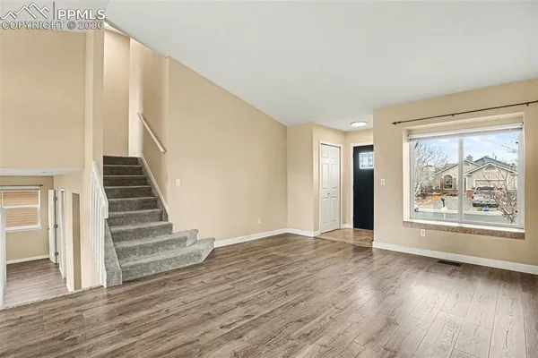 a view of an empty room with wooden floor and stairs