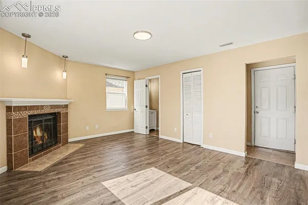 a view of an empty room with wooden floor fireplace and a window