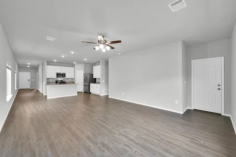 a view of an empty room and kitchen with wooden floor