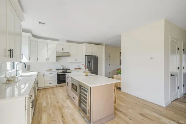 a open kitchen with a stove a sink a refrigerator and white cabinets with wooden floor