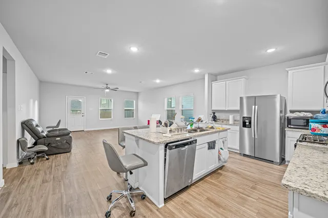 a kitchen with stainless steel appliances granite countertop a stove top oven a refrigerator a dining table and chairs with wooden floor