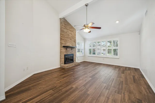 an empty room with wooden floor fireplace and windows