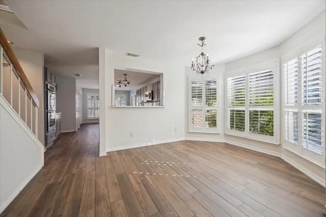an empty room with wooden floor chandelier and windows
