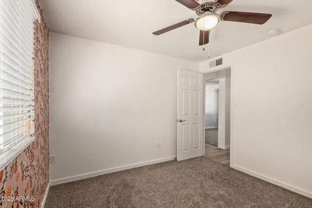 an empty room with a chandelier fan and windows