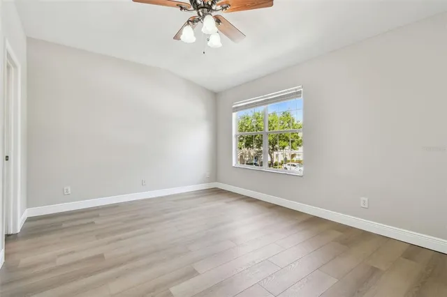 an empty room with wooden floor fan and windows
