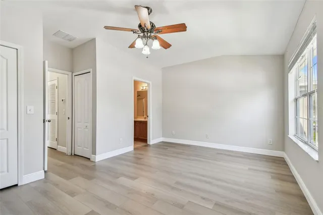 a view of an empty room with wooden floor and a ceiling fan