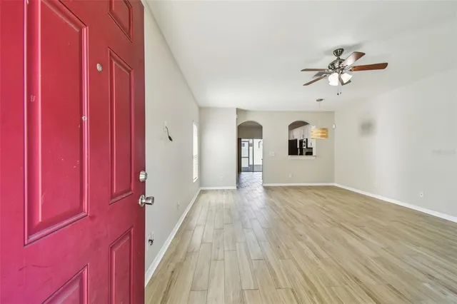 an empty room with wooden floor chandelier fan and windows