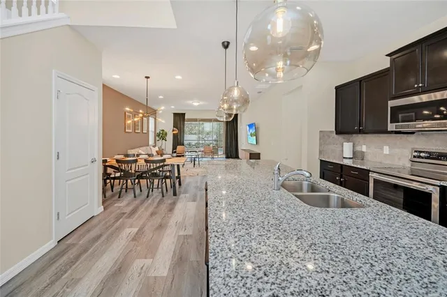 a kitchen with stainless steel appliances granite countertop a stove top oven a sink dishwasher a dining table and chairs with wooden floor