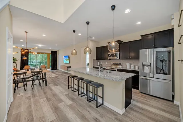 a kitchen with stainless steel appliances granite countertop a stove a refrigerator a kitchen island a dining table and chairs with wooden floor