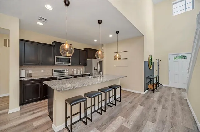 a kitchen with stainless steel appliances a stove top oven a sink dishwasher a refrigerator and a dining table with wooden floor