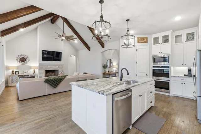 a kitchen with stainless steel appliances granite countertop a sink dishwasher a stove and a refrigerator with wooden floor