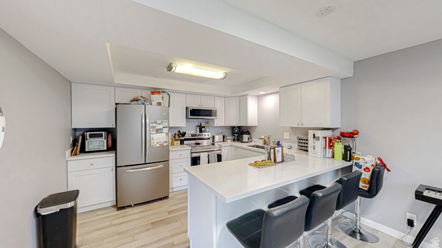 630 1100 West Provo, UT 84601 - Photo 24 of 64 Modern kitchen featuring white cabinetry, stainless steel appliances, light-toned wood-finish flooring, and a peninsula with countertop seating