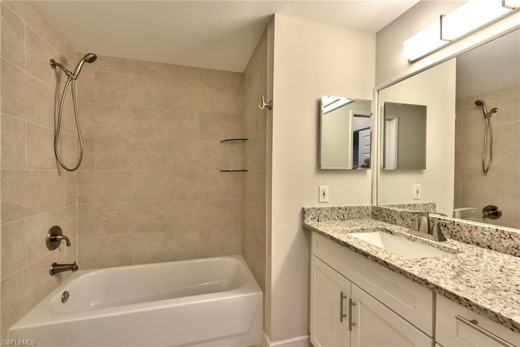 1200 Reserve Way, Unit 106 Naples, FL 34105 - Photo 13 of 31 a bathroom with a granite countertop sink a mirror and a bathtub