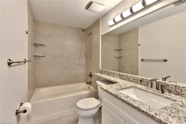 a bathroom with a granite countertop bathtub shower sink vanity mirror and toilet