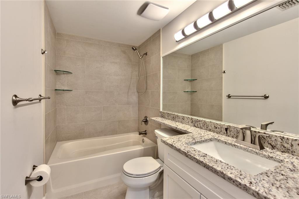 1200 Reserve Way, Unit 106 Naples, FL 34105 - Photo 14 of 31 a bathroom with a granite countertop bathtub shower sink vanity mirror and toilet