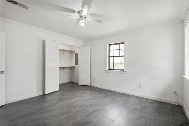 an empty room with chandelier fan and windows