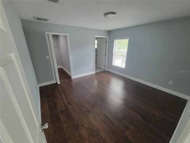 a view of an empty room with wooden floor and a window
