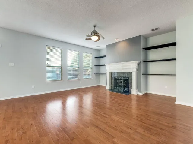 an empty room with wooden floor fireplace and windows