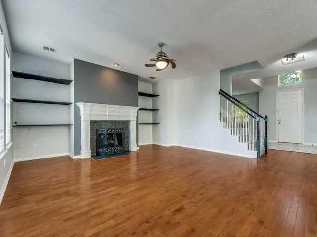 a view of an empty room with wooden floor fireplace and a window