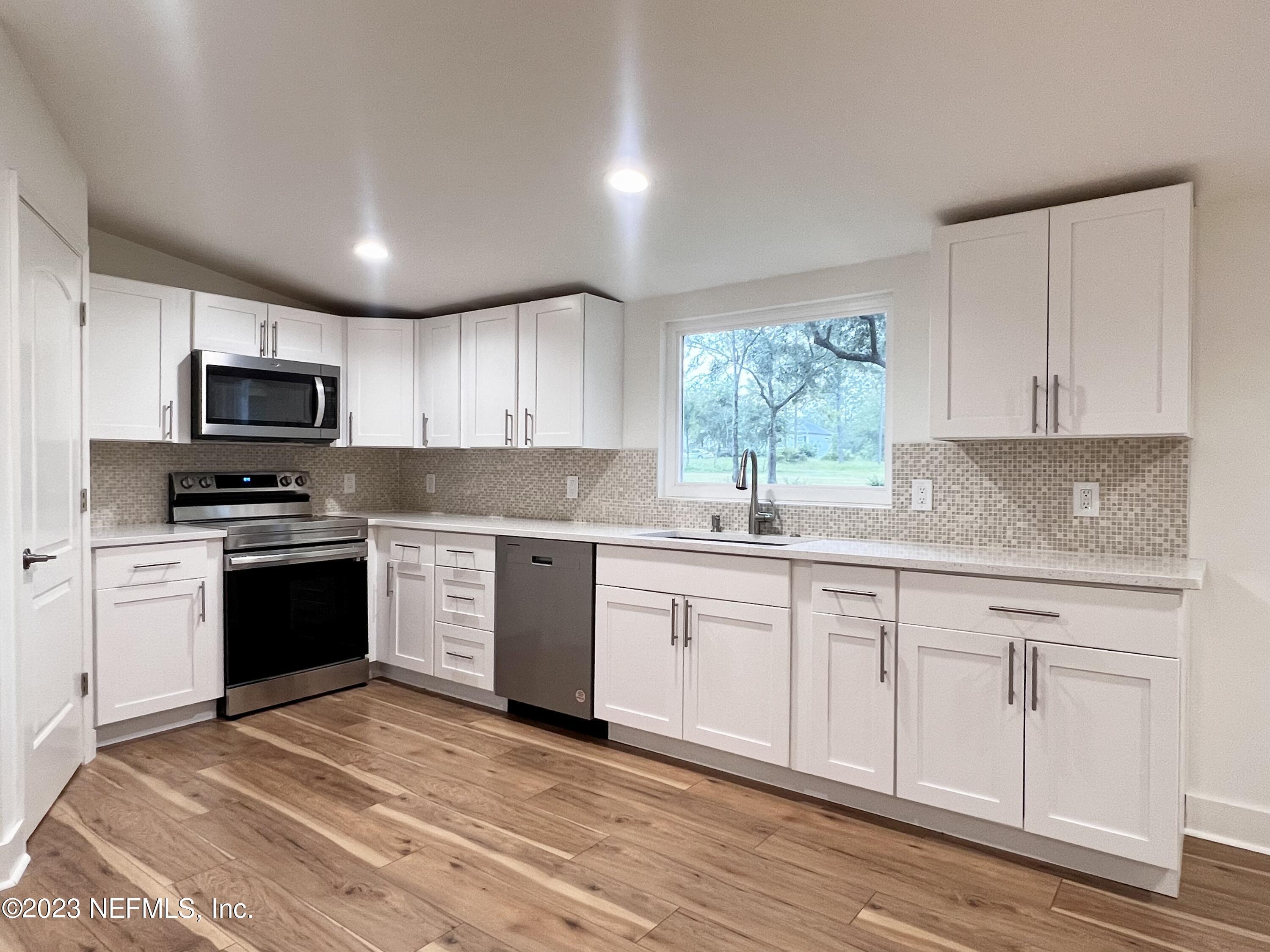 a kitchen with granite countertop white cabinets a window a sink and appliances