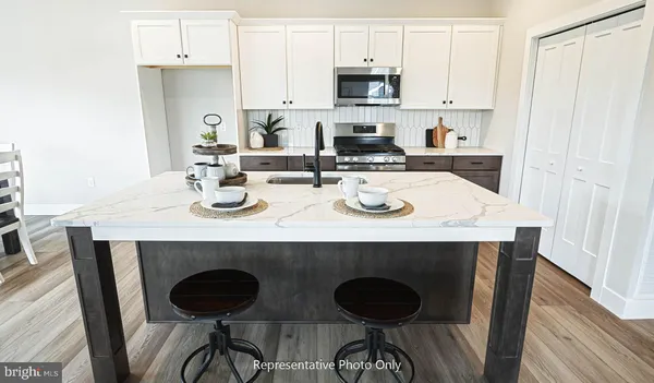 a kitchen with stainless steel appliances granite countertop a stove a sink a refrigerator and white cabinets with wooden floor