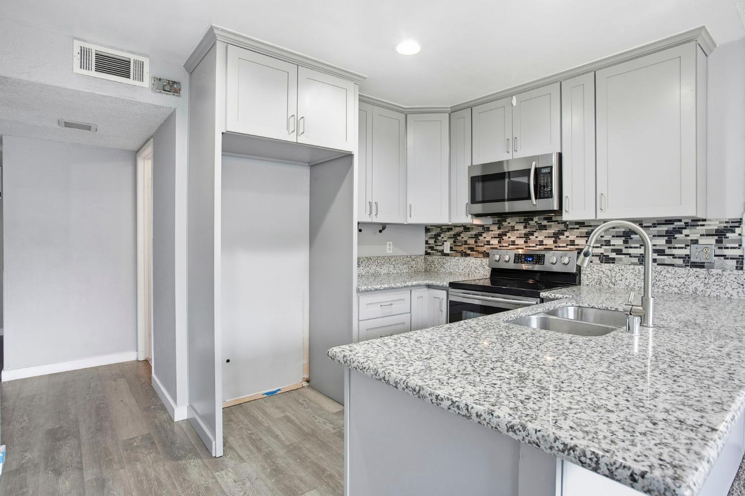5805 Muldrow Road Sacramento, CA 95841 - Photo 3 of 27 kitchen with light stone counters, appliances with stainless steel finishes, decorative backsplash, light wood-type flooring, and a peninsula