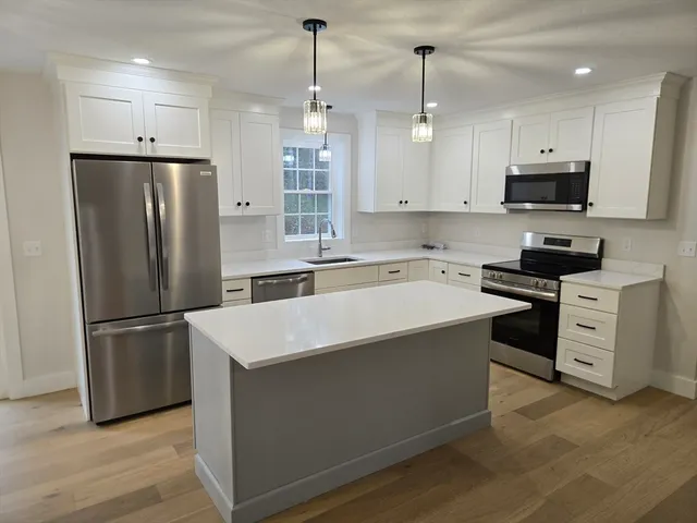 a kitchen that has a refrigerator a stove and white cabinets with wooden floor