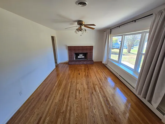a view of a livingroom with wooden floor a ceiling fan and windows