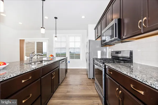 a kitchen with stainless steel appliances kitchen island granite countertop a stove a sink dishwasher a refrigerator and a microwave oven with wooden floor