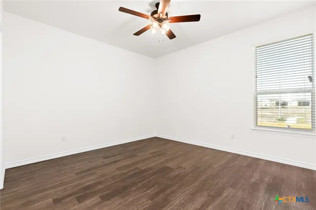 an empty room with wooden floor fan and windows
