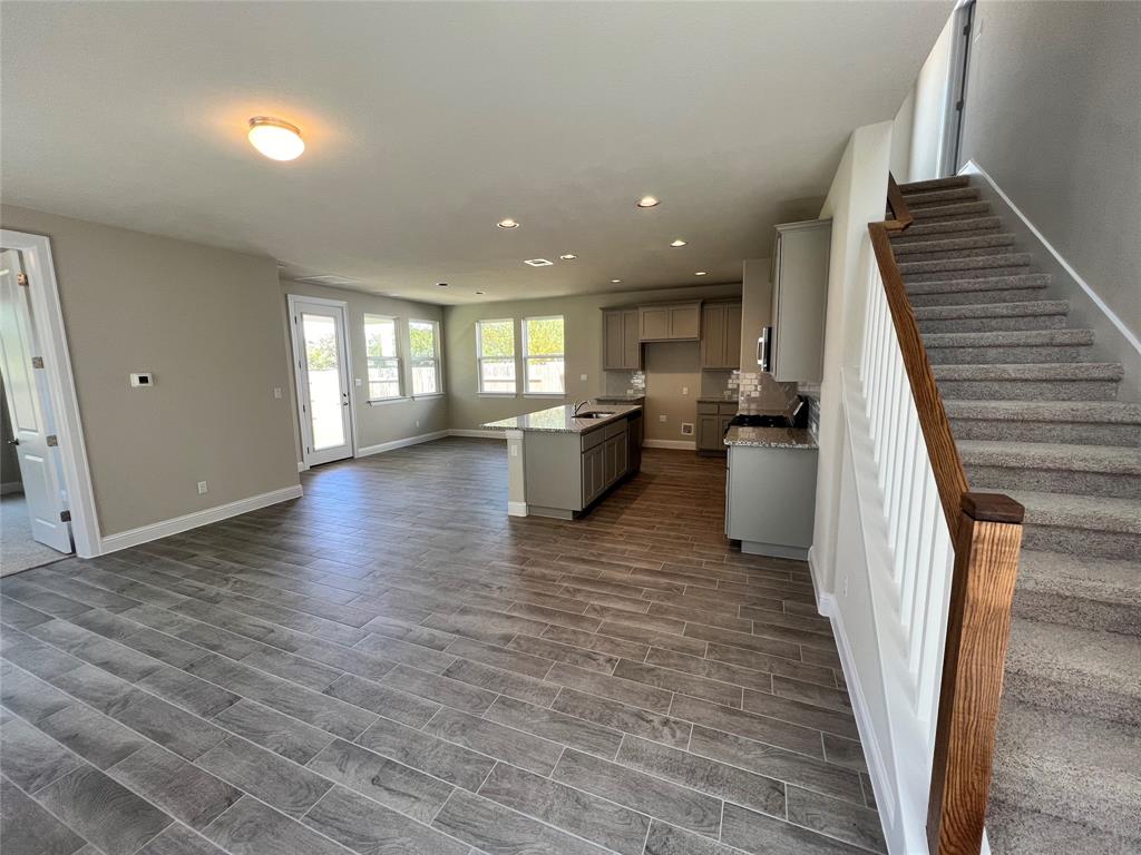 128 Free Stone Drive Georgetown, TX 78628 - Photo 20 of 29 Open-concept living space featuring wood-finish tile flooring, a kitchen island with a double sink, granite countertops, and stainless steel appliances