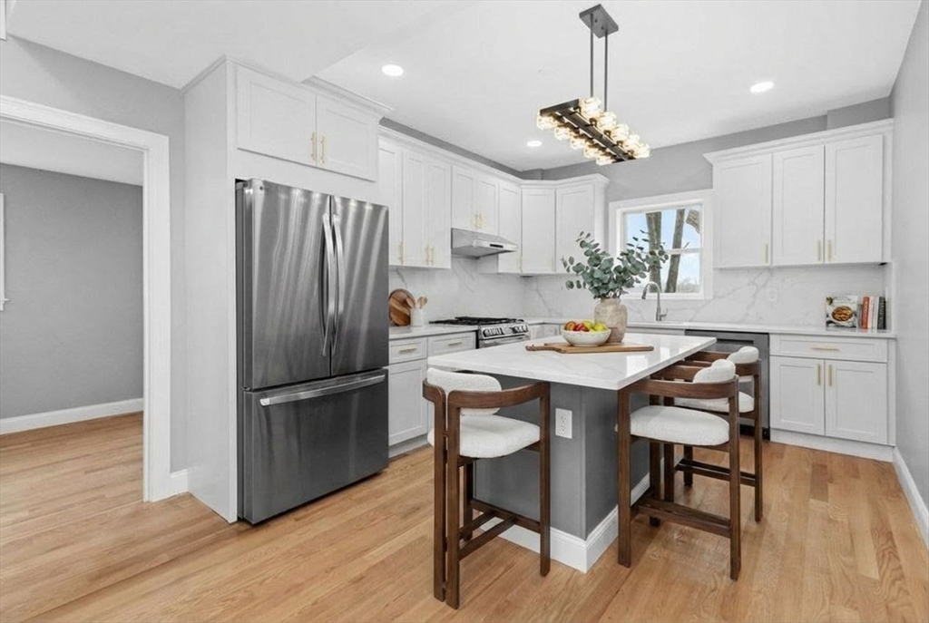 66 Stanley Street Boston, MA 02125 - Photo 4 of 42 a kitchen with kitchen island a refrigerator a stove a dining table and chairs with wooden floor