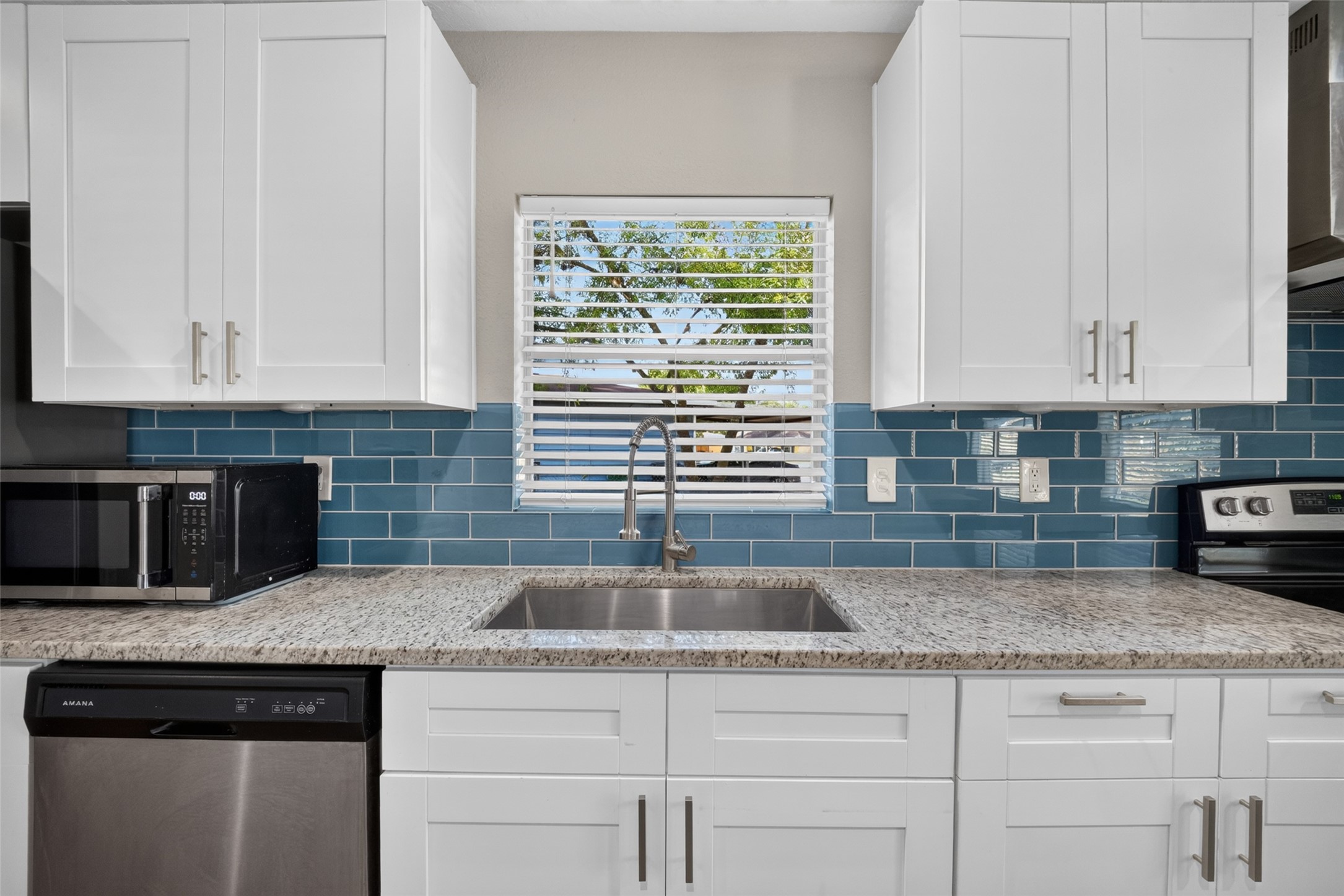 5217 Pomander Road Houston, TX 77021 - Photo 6 of 18 Updated kitchen featuring crisp white cabinetry, granite countertops, stainless steel appliances, and a stylish blue tile backsplash.