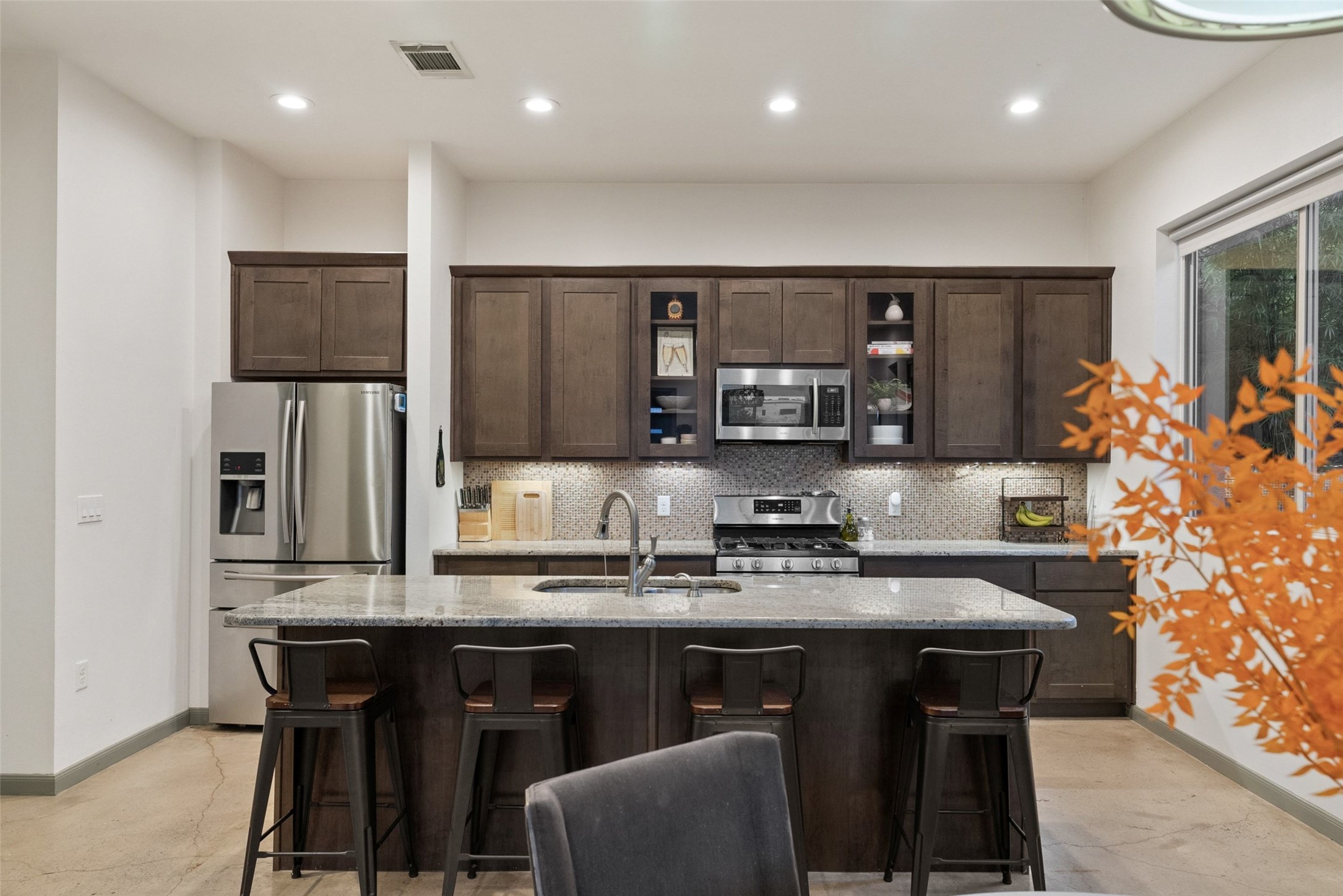A contemporary kitchen showcasing dark wood cabinetry, a granite island with seating, and sleek stainless steel appliances.