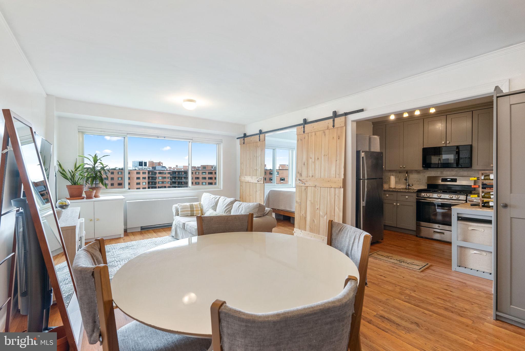 a living room with stainless steel appliances a dining table wooden floor and a kitchen view