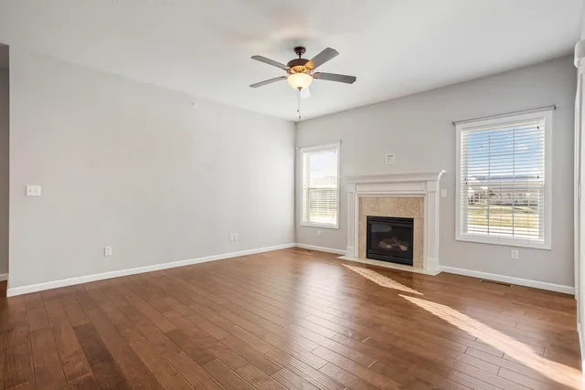 an empty room with wooden floor fireplace and windows