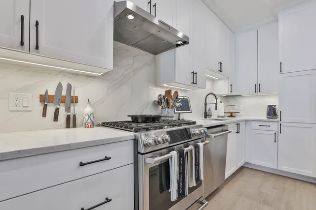 a kitchen with stainless steel appliances granite countertop a sink a stove and white cabinets