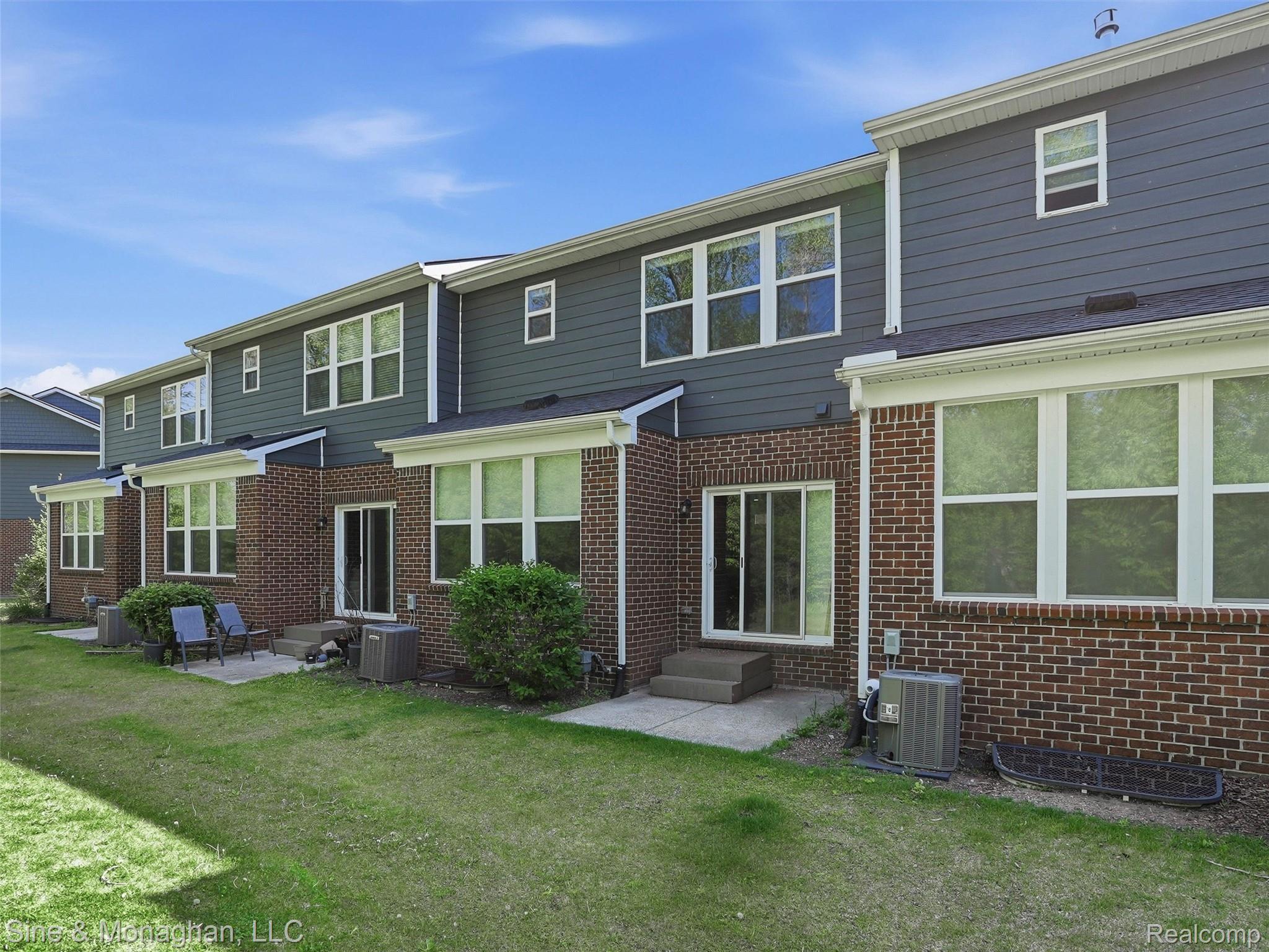 24827 Ivy Road Novi, MI 48375 - Photo 34 of 38 Rear exterior featuring brick and horizontal siding, multiple white-framed windows, and sliding glass door access to concrete patios