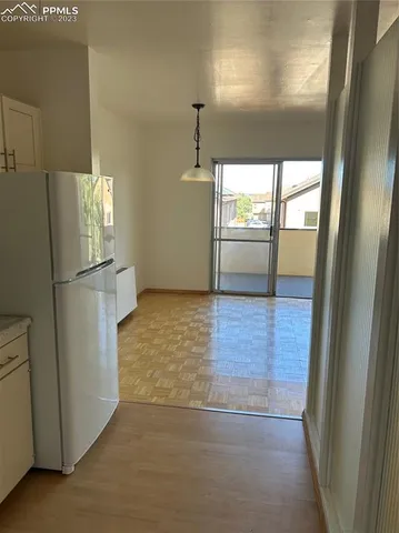 a view of a refrigerator in kitchen and an empty room with wooden floor