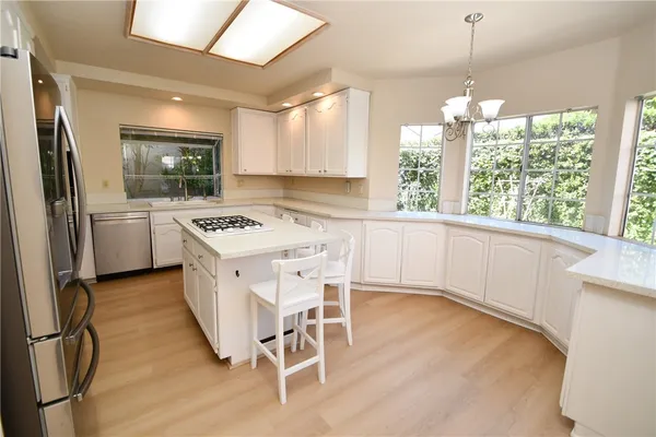 a kitchen with stainless steel appliances granite countertop a stove a sink dishwasher a refrigerator with white cabinets and wooden floor