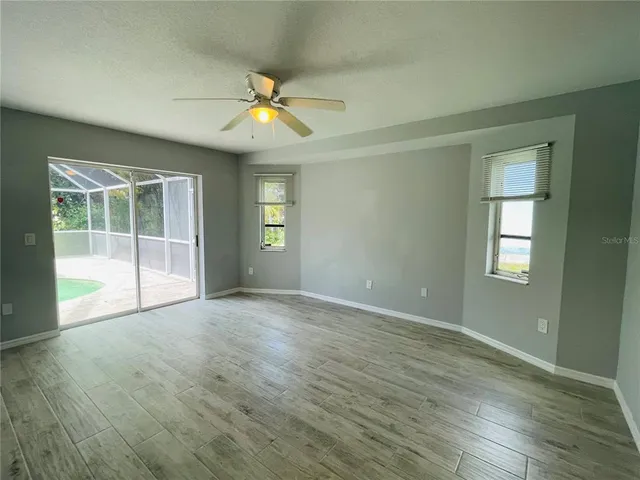 an empty room with wooden floor fan and windows