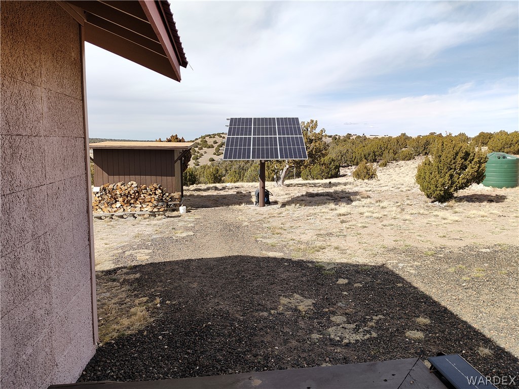 15 County Road Concho, AZ 85924 - Photo 67 of 93 Outdoor area featuring a freestanding solar panel array, a brown storage shed with a stacked woodpile, and a green water storage tank